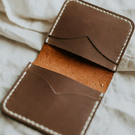A brown leather minimalist bifold wallet open to show its interior compartments and card slots, highlighting its simple design and craftsmanship.