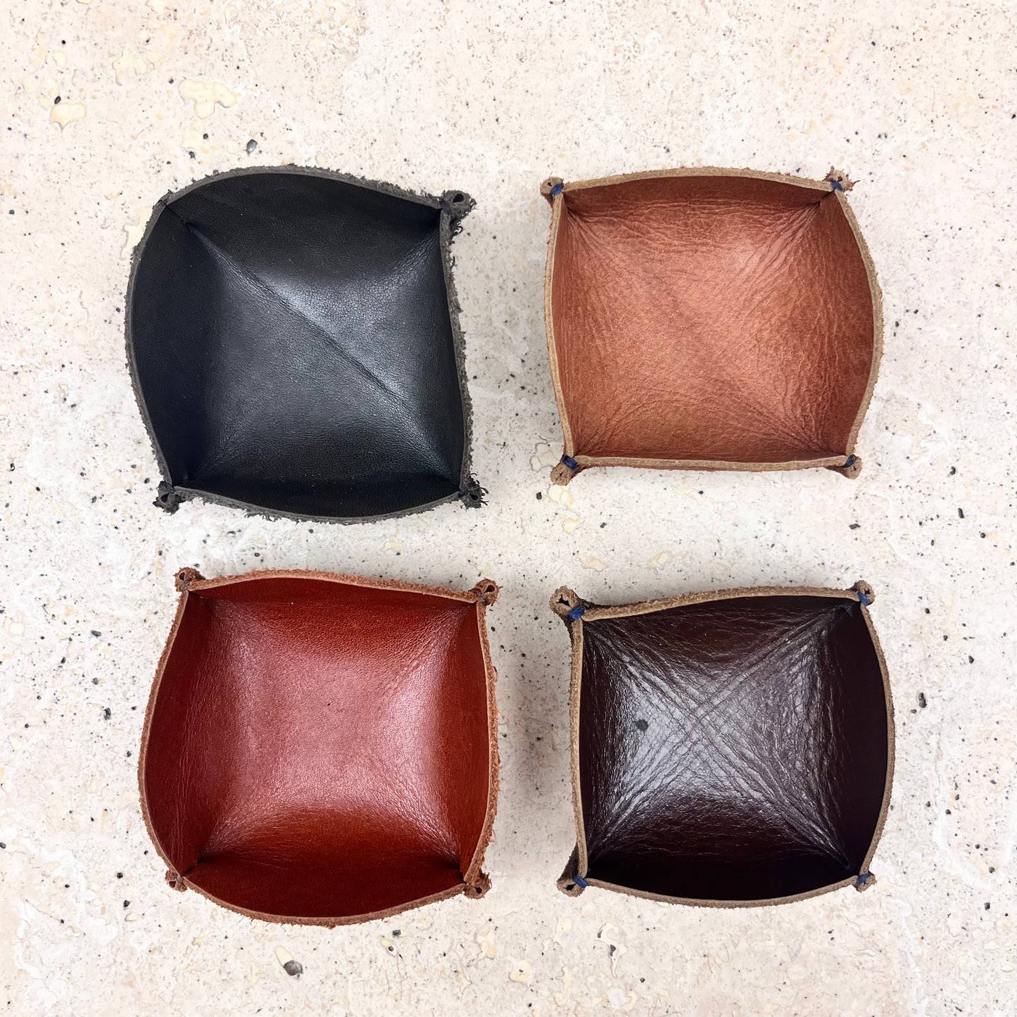 Four leather ring trays in different colors (black, brown, tan brown, and burgundy) arranged together, showcasing the variety of options available.