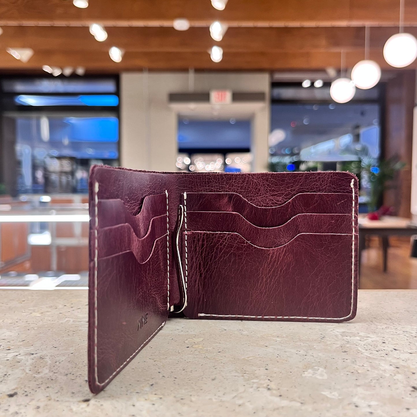 A burgundy leather bifold wallet open, displaying multiple card slots and a spring money clip.