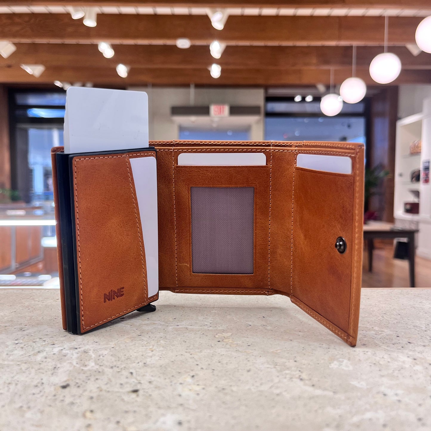 A tan brown NINE Leather & Watch Mechanical Wallet partially open, showcasing its card ejection mechanism and premium leather craftsmanship.