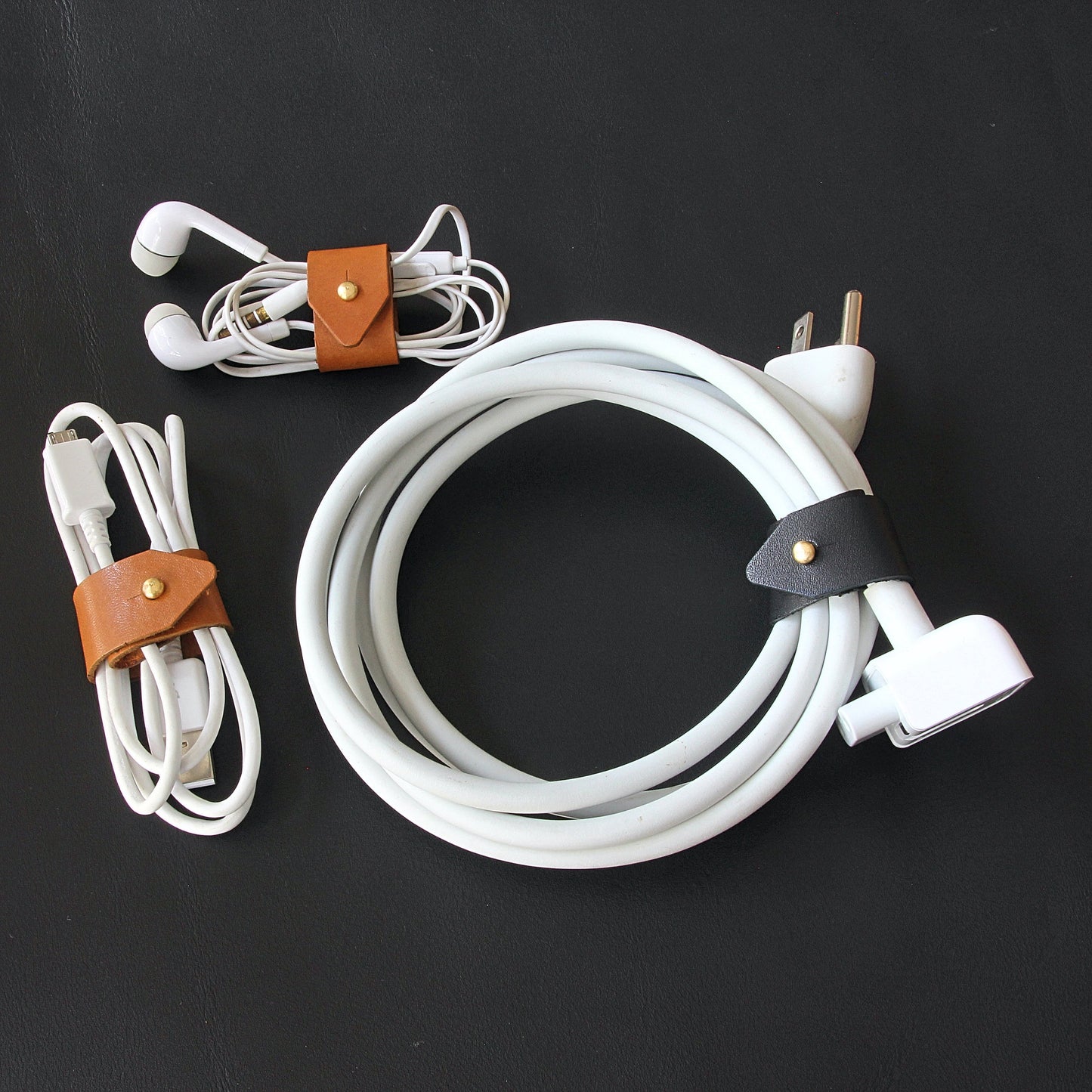 A brown leather cord wrap organizing a Macbook charger cable.