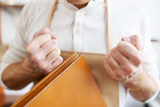 A photo of a skilled artisan hand-stitching a leather bag, with sunlight streaming through the window and illuminating the rich texture of the leather and the meticulous craftsmanship.