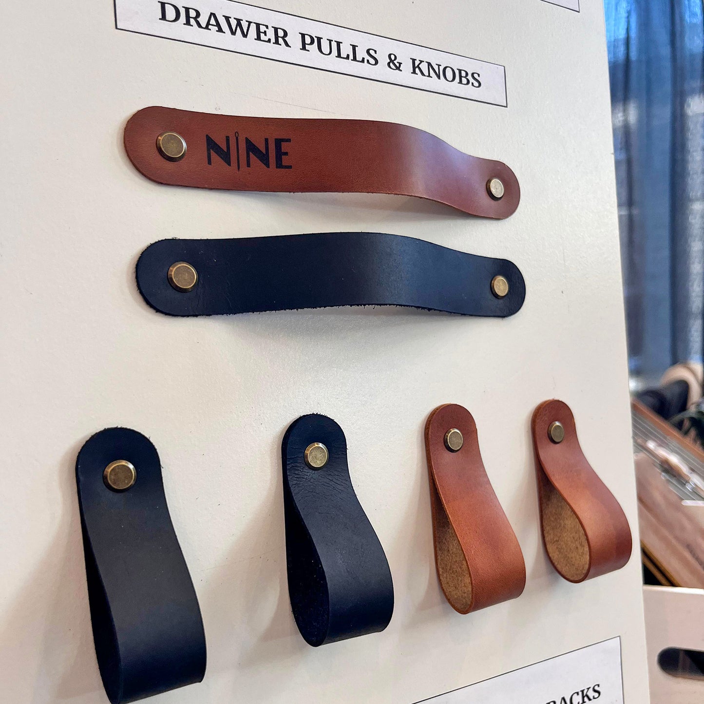 Close-up of tan and black full-grain leather cabinet pulls and loop knobs with professional brass hardware on a display at NINE in Independence.