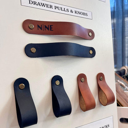 Close-up of tan and black full-grain leather cabinet pulls and loop knobs with professional brass hardware on a display at NINE in Independence.