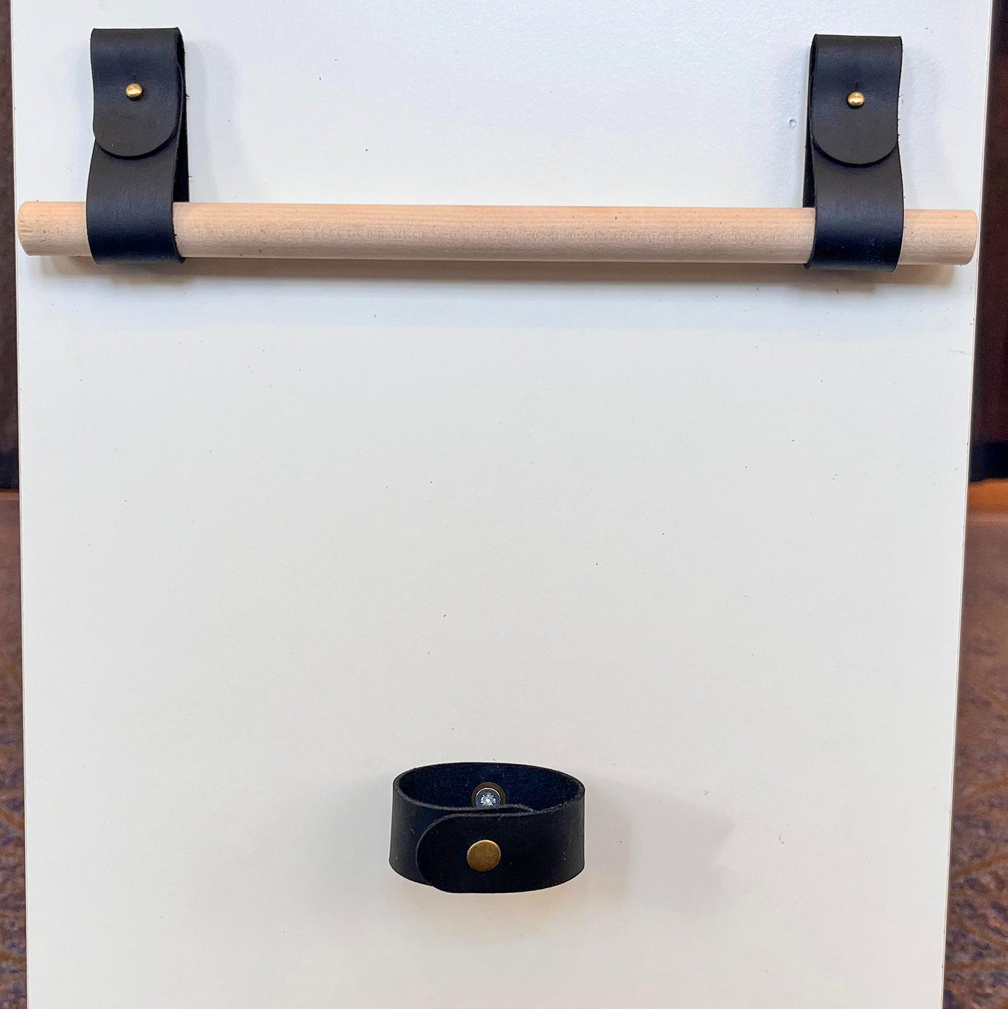 Custom black leather rod holders mounted with brass rivets supporting a wooden rod, with a matching leather tieback below.