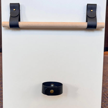 Custom black leather rod holders mounted with brass rivets supporting a wooden rod, with a matching leather tieback below.