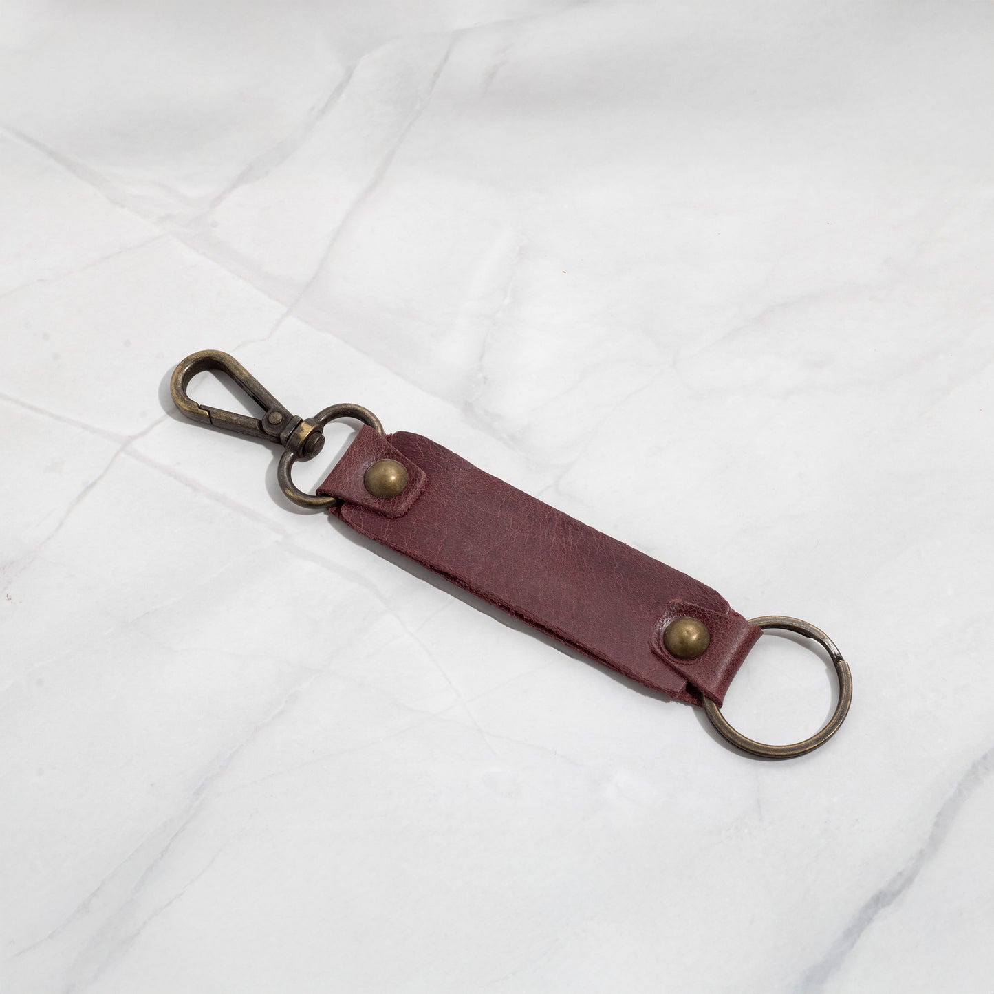 Deep burgundy leather key fob with brass rivets and a sturdy swivel snap hook, photographed on a white background.