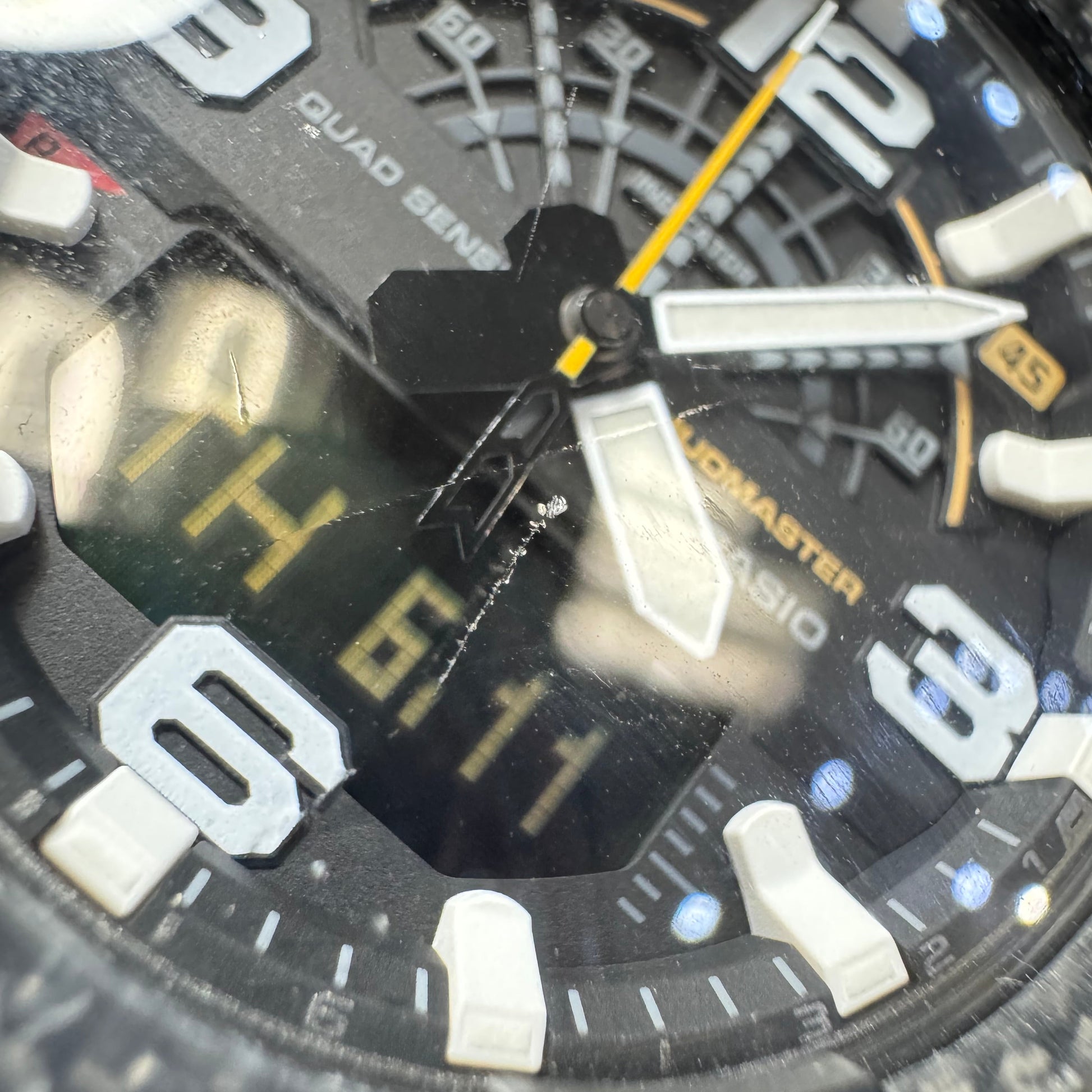 Extreme close-up of the Casio G-Shock analog-digital watch face, highlighting a minor, faint cosmetic scratch on the center of the crystal glass.