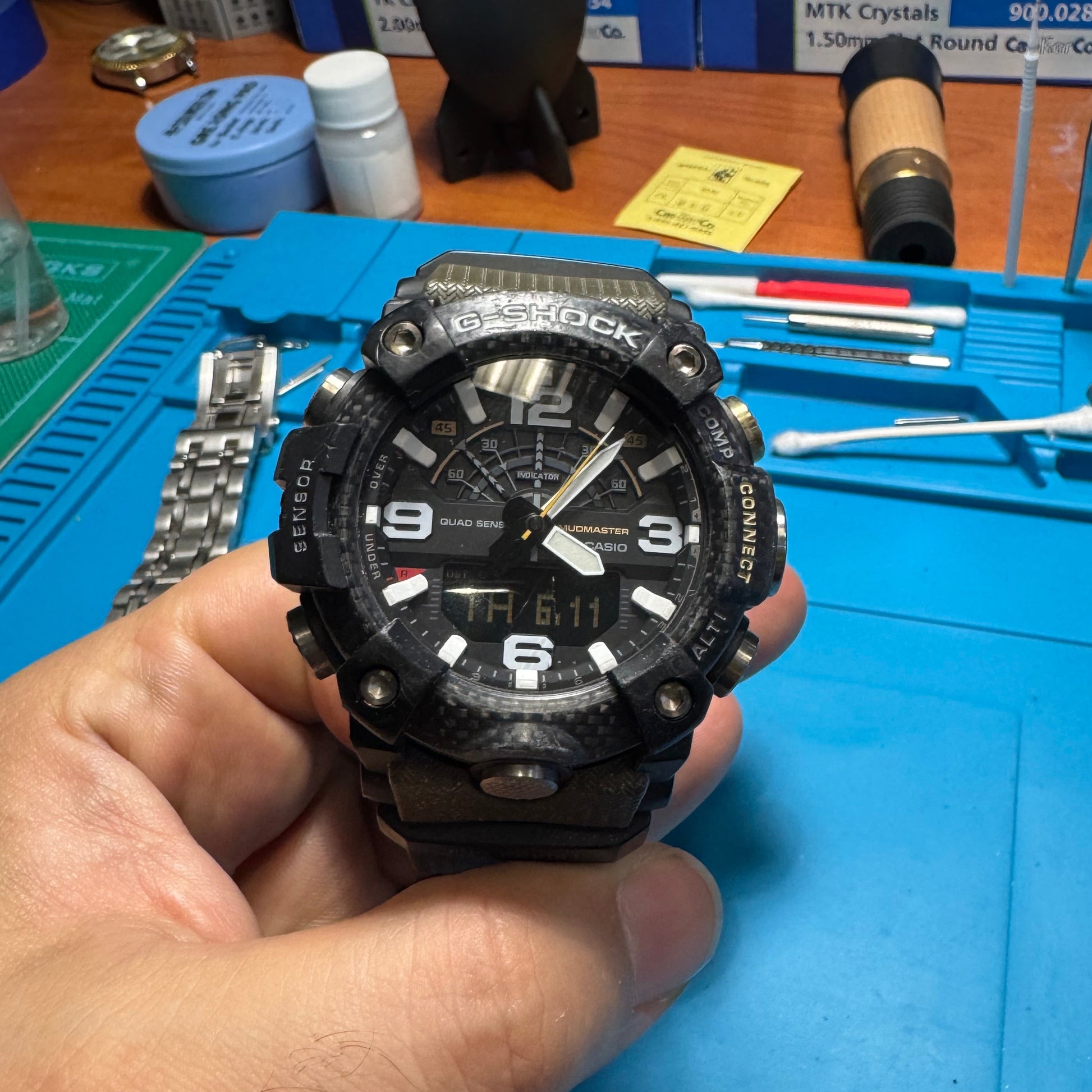 Front angle view of the rugged Casio G-Shock Mudmaster watch held in hand, showcasing the textured carbon core guard bezel and analog-digital dial.