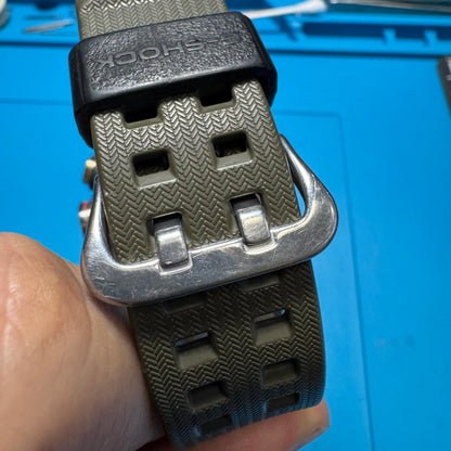 Close-up detailing the heavy-duty olive green resin strap, black G-Shock branded keeper loop, and polished stainless steel buckle.