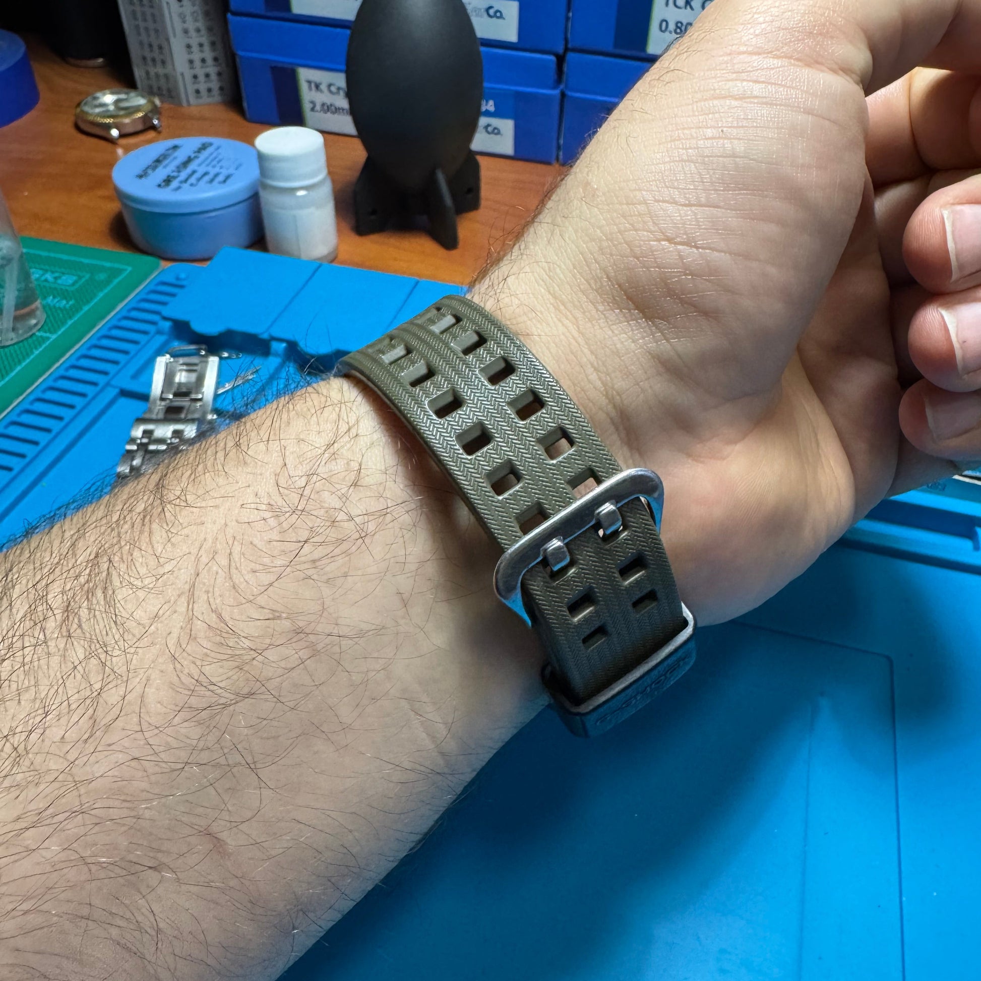 Underside view of the Casio G-Shock watch worn on a wrist, showing the secure fit of the olive green textured resin strap and stainless steel buckle.