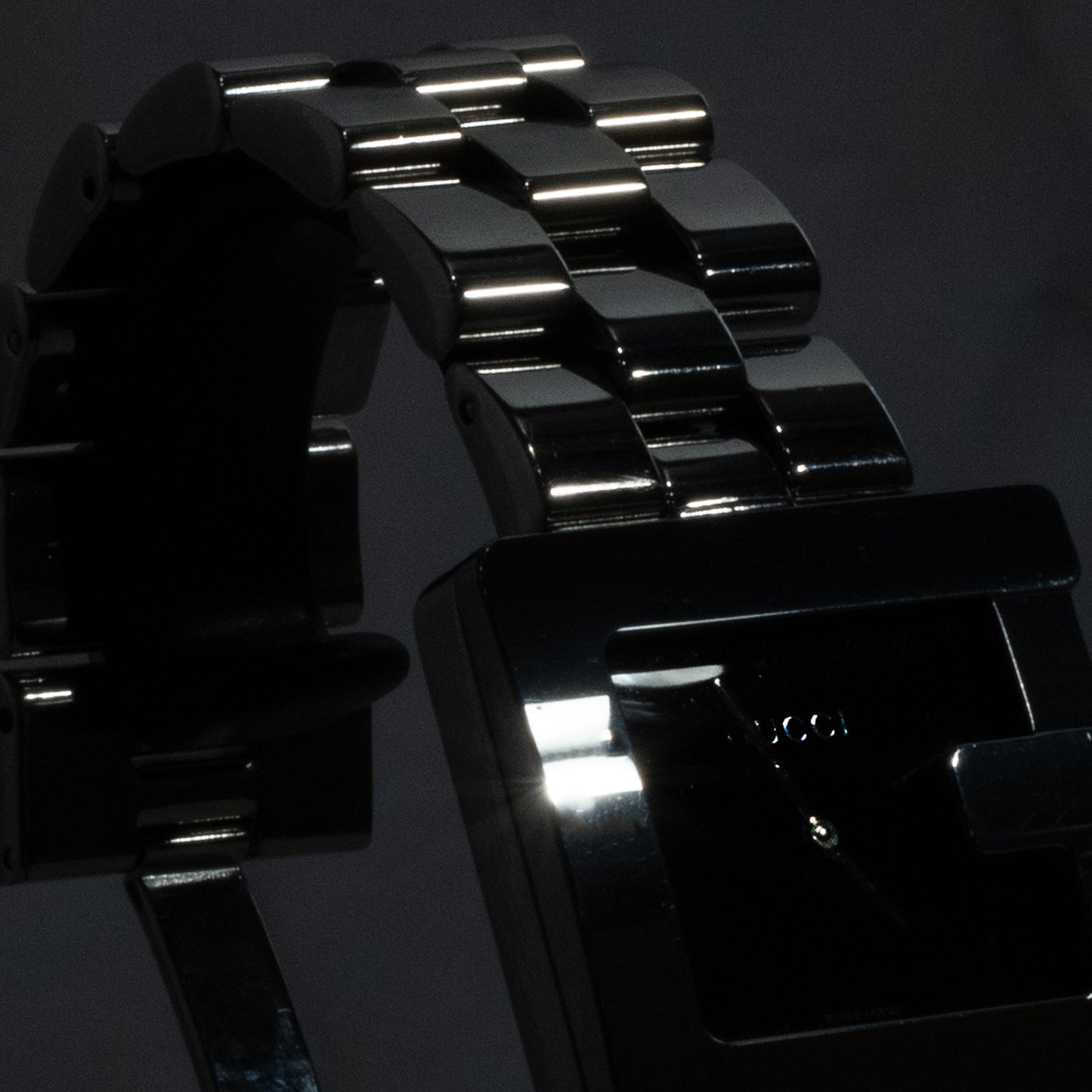 A dramatic, high-contrast close-up of the polished multi-link stainless steel bracelet and the signature "G" case of a refurbished vintage Gucci 3600M watch.