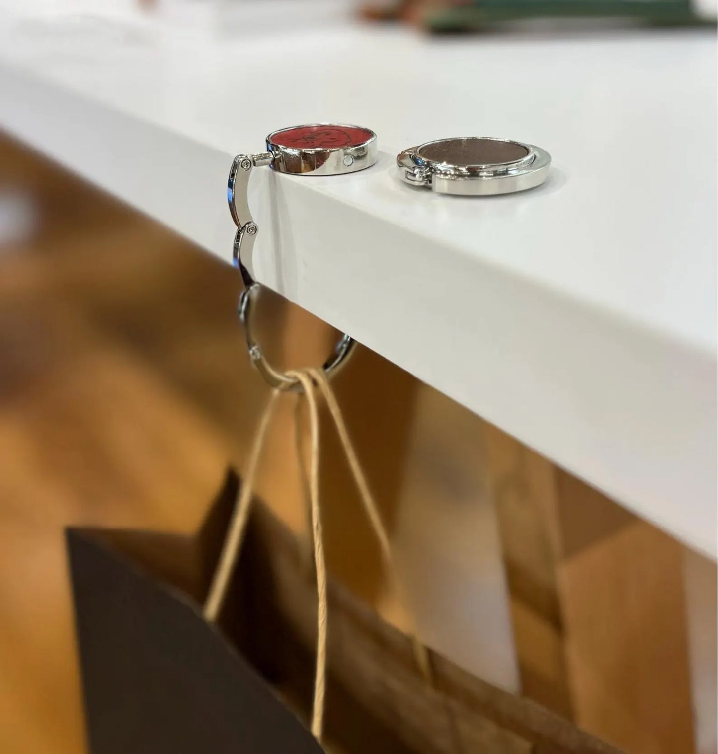 Two leather bag hangers on a white table: one unfolded in use with red leather, and one folded flat into a compact disc with brown leather.