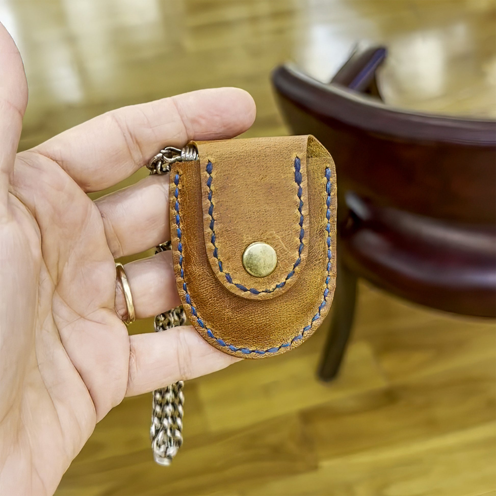 Hand holding a closed leather pocket watch sleeve, highlighting the compact design and tight fit that protects the watch without adding bulk.