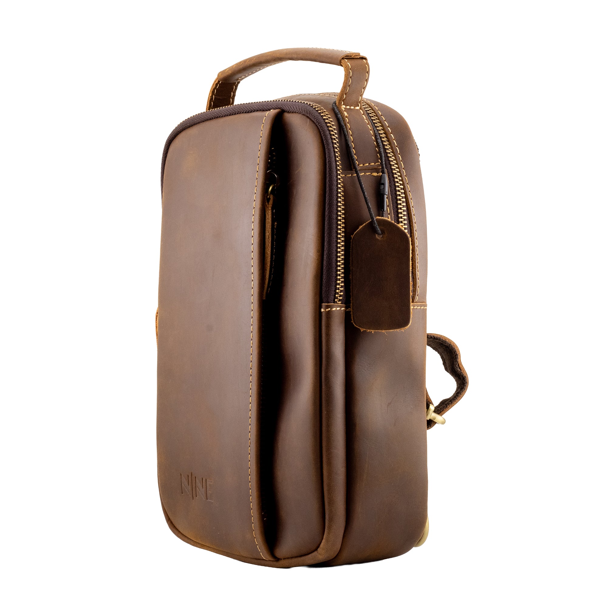 Angled profile view of the NINE Leather Crazy Horse Sling Bag in brown, showcasing the rich patina of the leather, dual zippered main compartments, and heavy-duty stitching isolated on a white background.