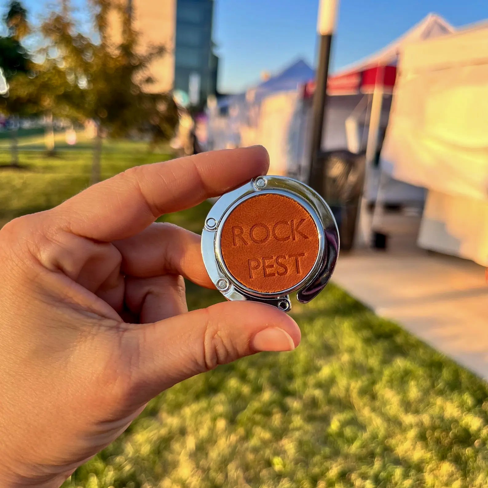 Hand holding a round leather bag hanger with "ROCK PEST" monogram cold stamp horizontally on a tan leather inlay.