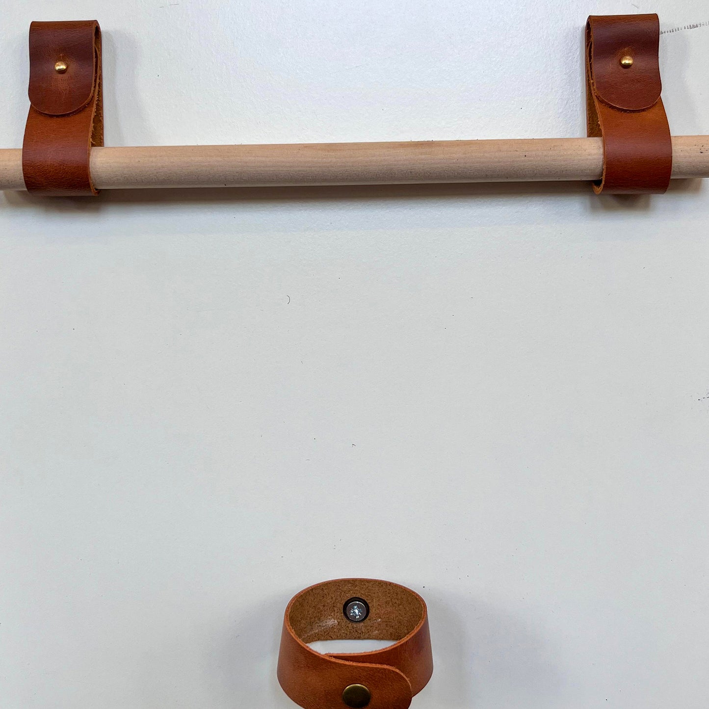 Front-facing view of professional tan leather rod holders supporting a wooden rod with a coordinating leather tieback.