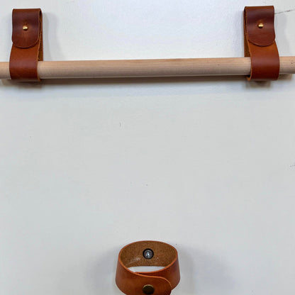 Front-facing view of professional tan leather rod holders supporting a wooden rod with a coordinating leather tieback.