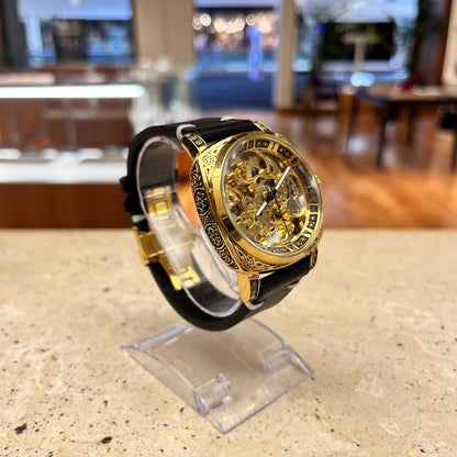 Customized NINE automatic skeleton watch with a gold-colored engraved case, luminous display, and black handmade leather band with gold butterfly clasp, front angle view.