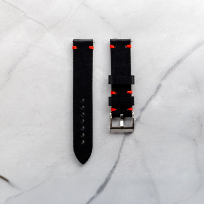 Top-down view of a handmade black full-grain leather watch band featuring vibrant red artisan stitching and a classic silver buckle on a marble background.