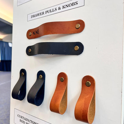 Angled view of professional leather home hardware display with black and tan pulls and knobs at NINE Leather & Watch in Independence, MO.