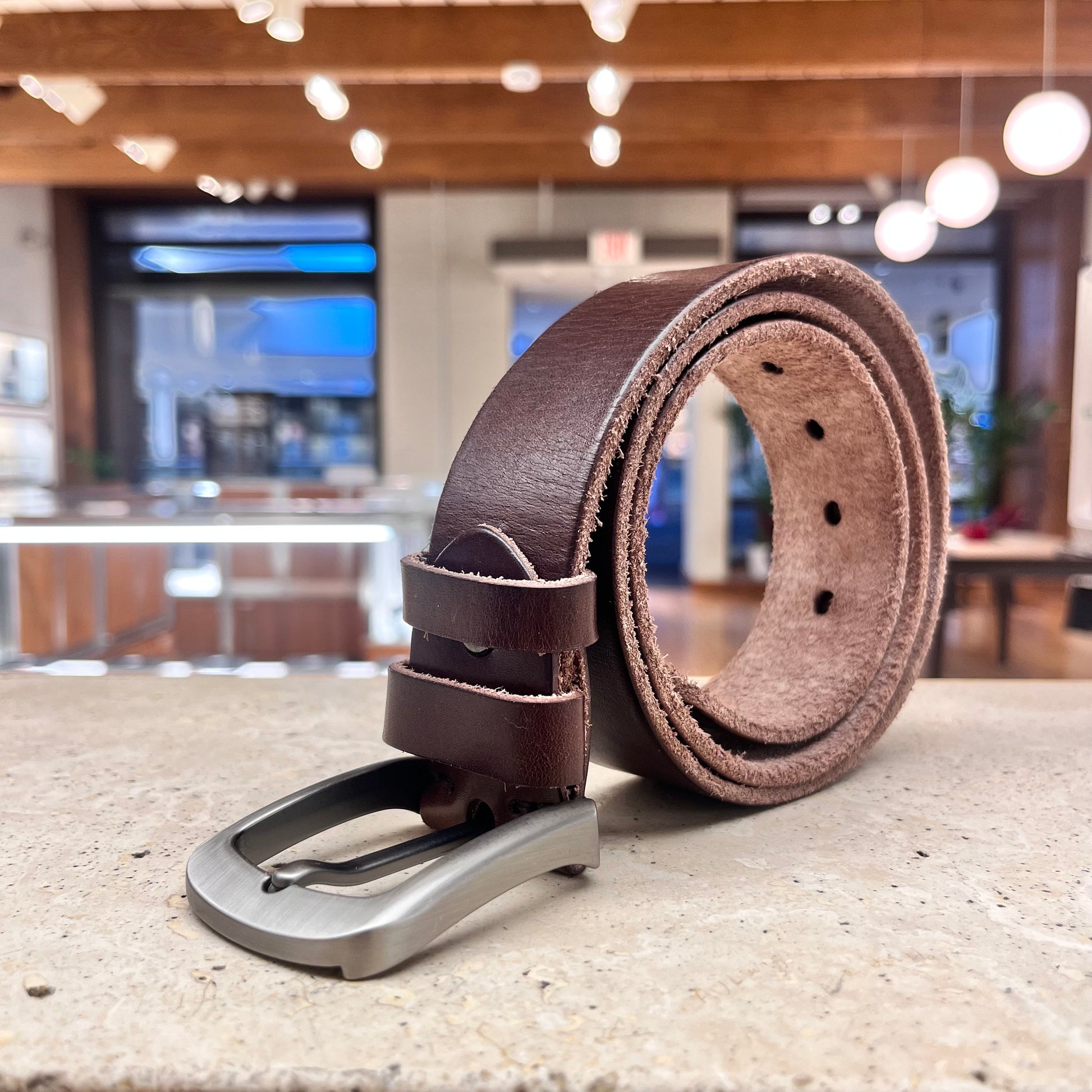  A rich brown leather belt with a silver buckle, highlighting its classic style and handcrafted quality.