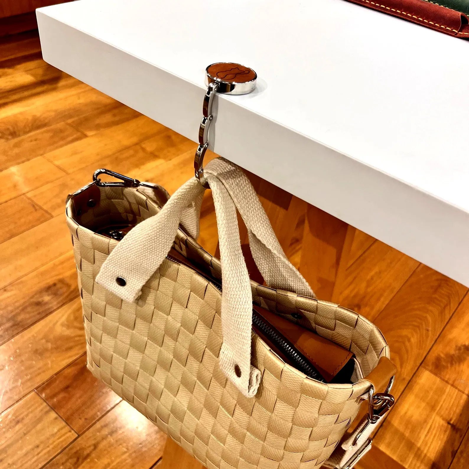 A woven tote bag hanging securely from a white table using a personalized leather purse hook, demonstrating the weight capacity.
