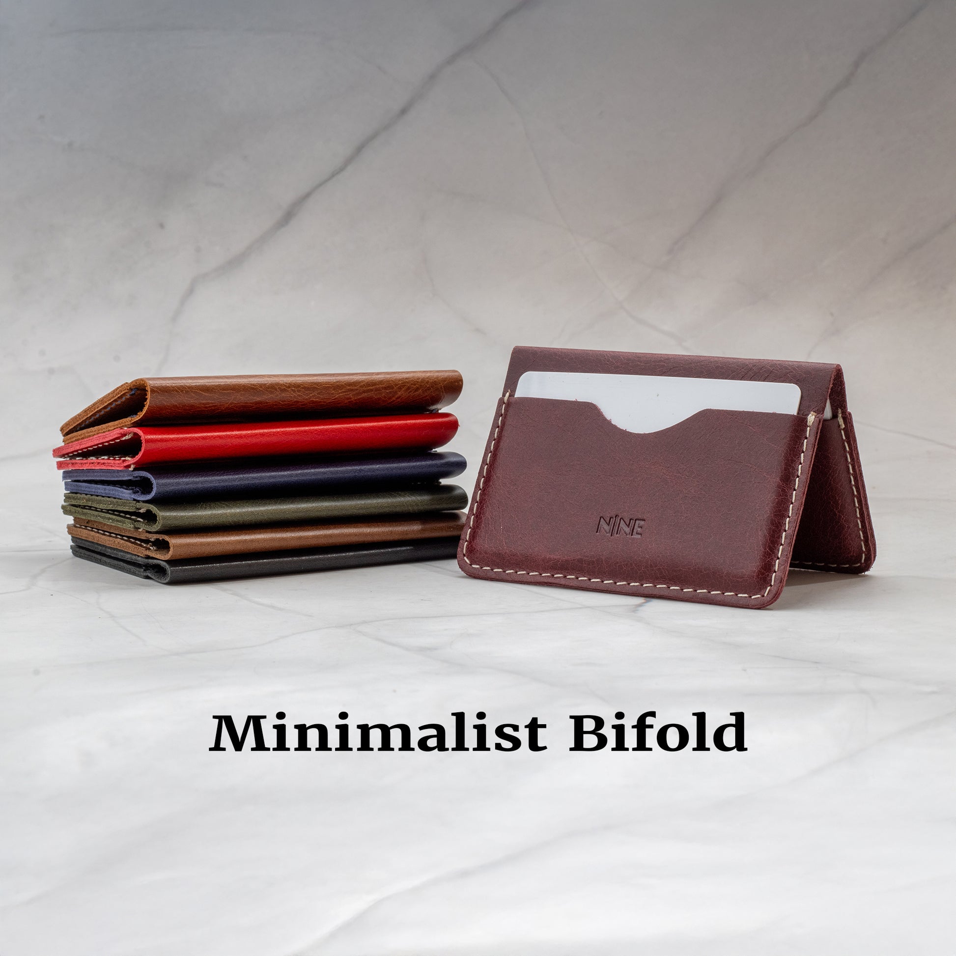 Stack of Minimalist Bifold wallets in various colors (Red, Brown, Burgundy, Green), next to an open Burgundy wallet with white stitching.