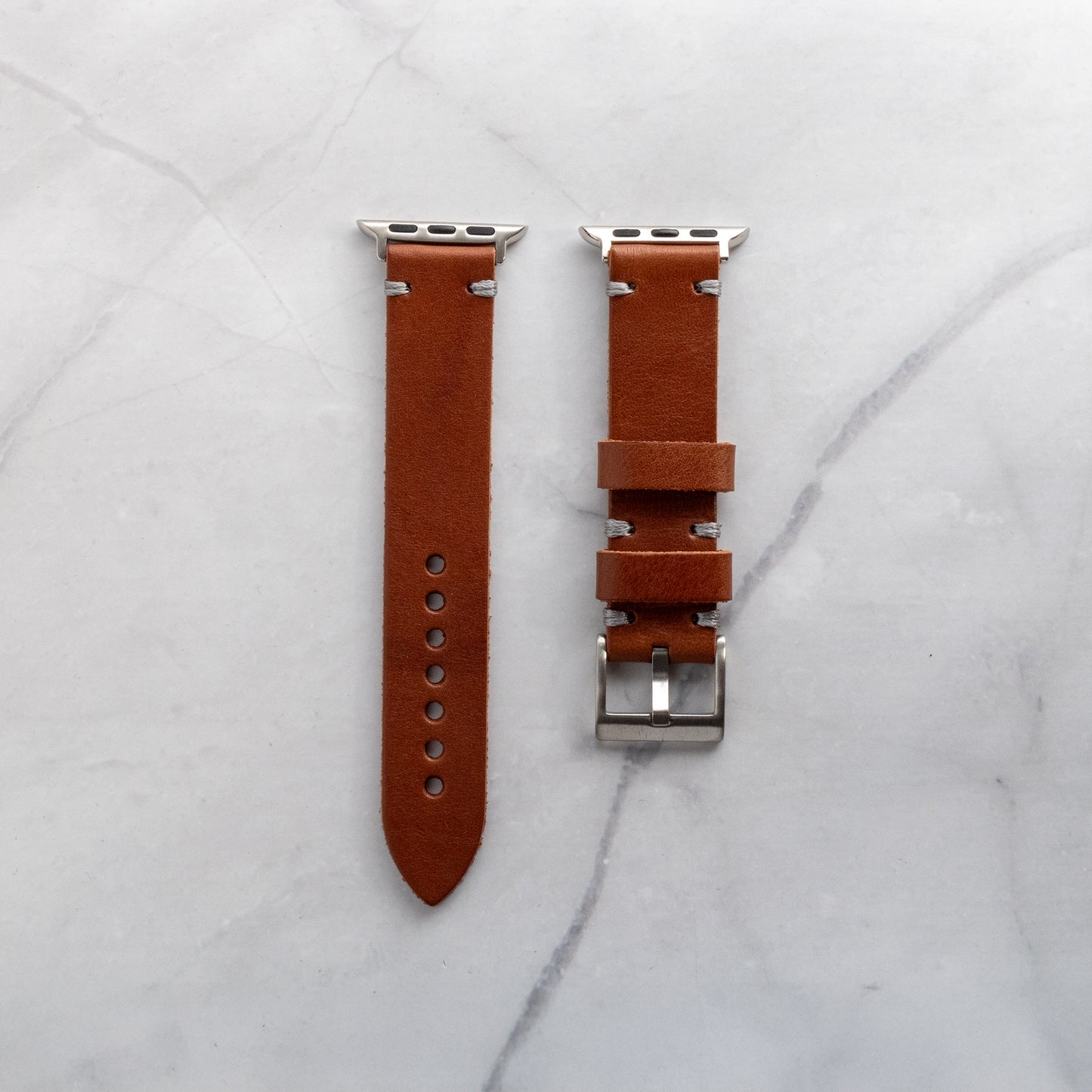 Bespoke tan full-grain leather Apple Watch band with grey hand-finished stitching and silver adapters, highlighting the natural leather grain.