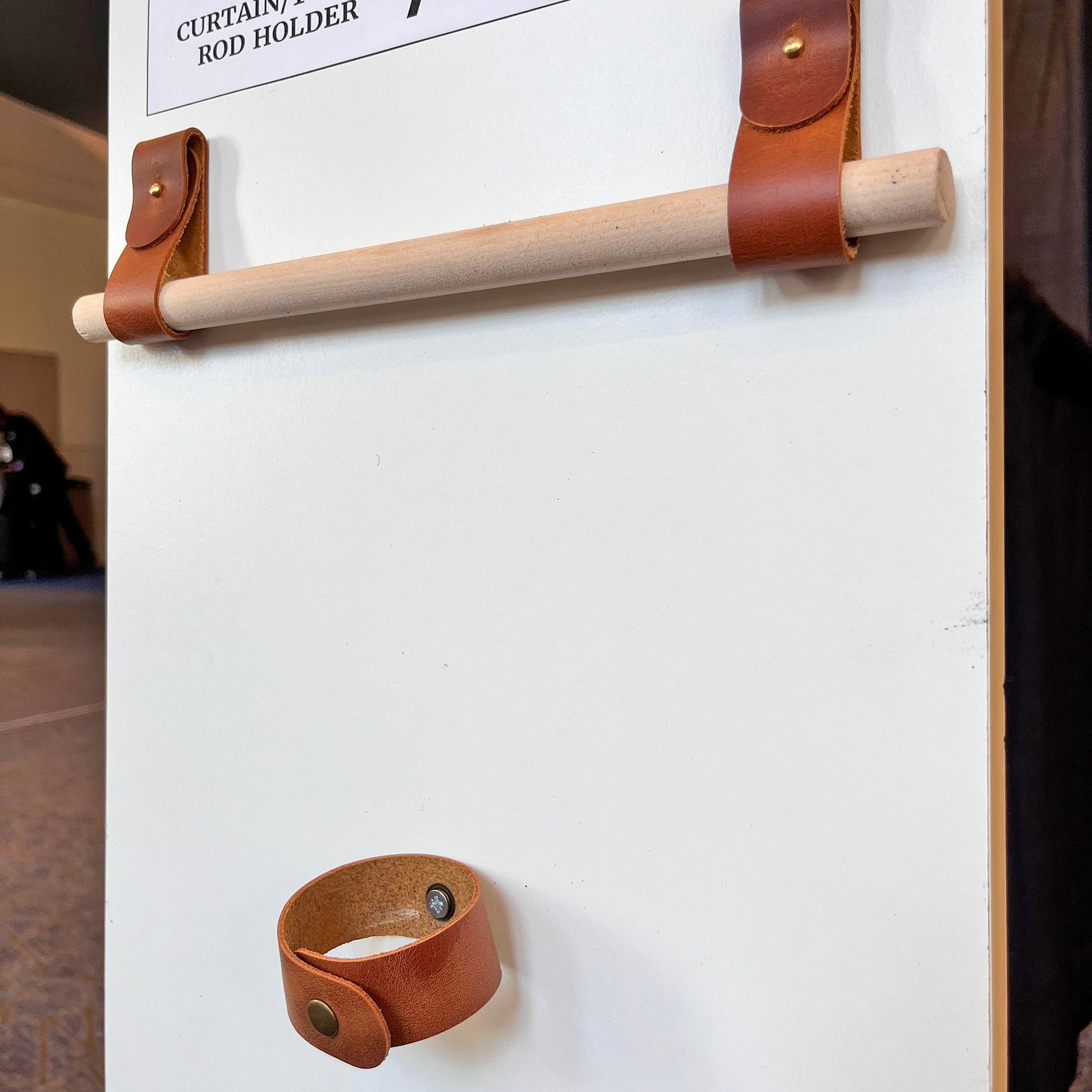 Angled view of tan full-grain leather rod holders and matching tieback on a white display board at the NINE workshop.