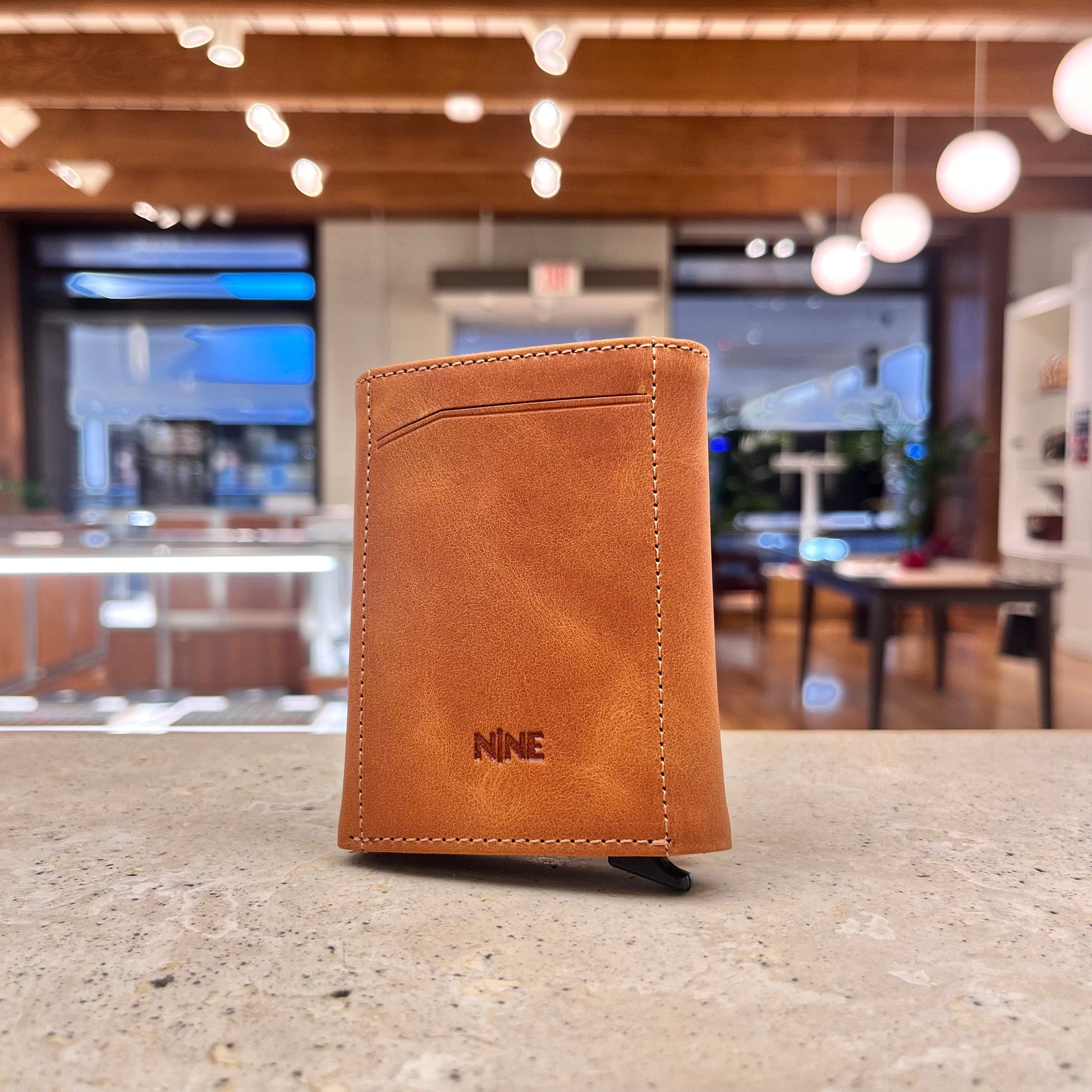 A tan brown NINE Leather & Watch Mechanical Wallet displayed against a blurred background, showcasing its rich color and sleek design.