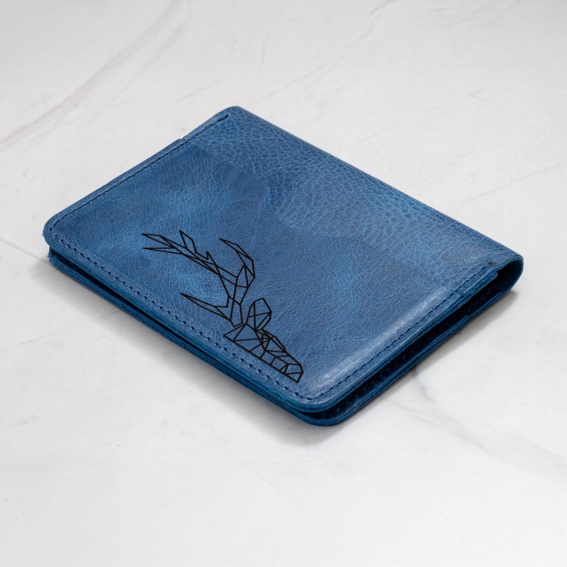 Close-up of a blue full-grain leather wallet with a laser-engraved geometric deer head design on the cover.