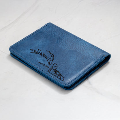 Close-up of a blue full-grain leather wallet with a laser-engraved geometric deer head design on the cover.