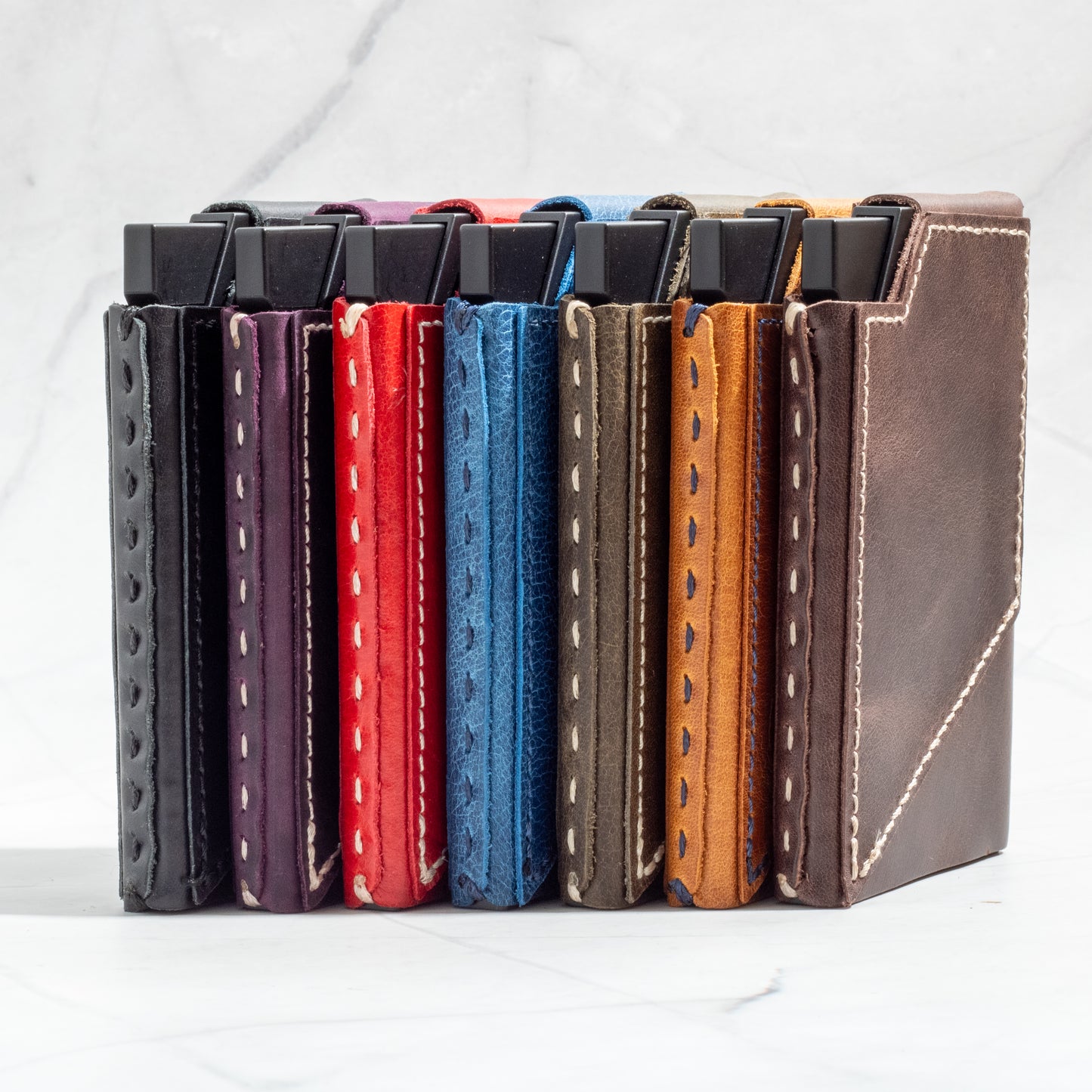 Close-up stack of various color NINE mechanical pop-up wallets highlighting detailed stitching on premium full-grain leather