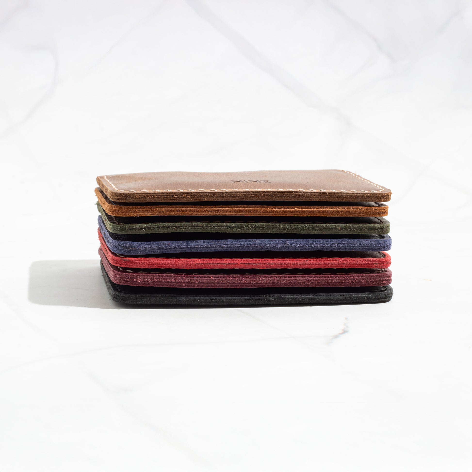 Stack of NINE Compact Card Wallets in various Full-Grain Leather colors, showcasing the ultra-slim profile.