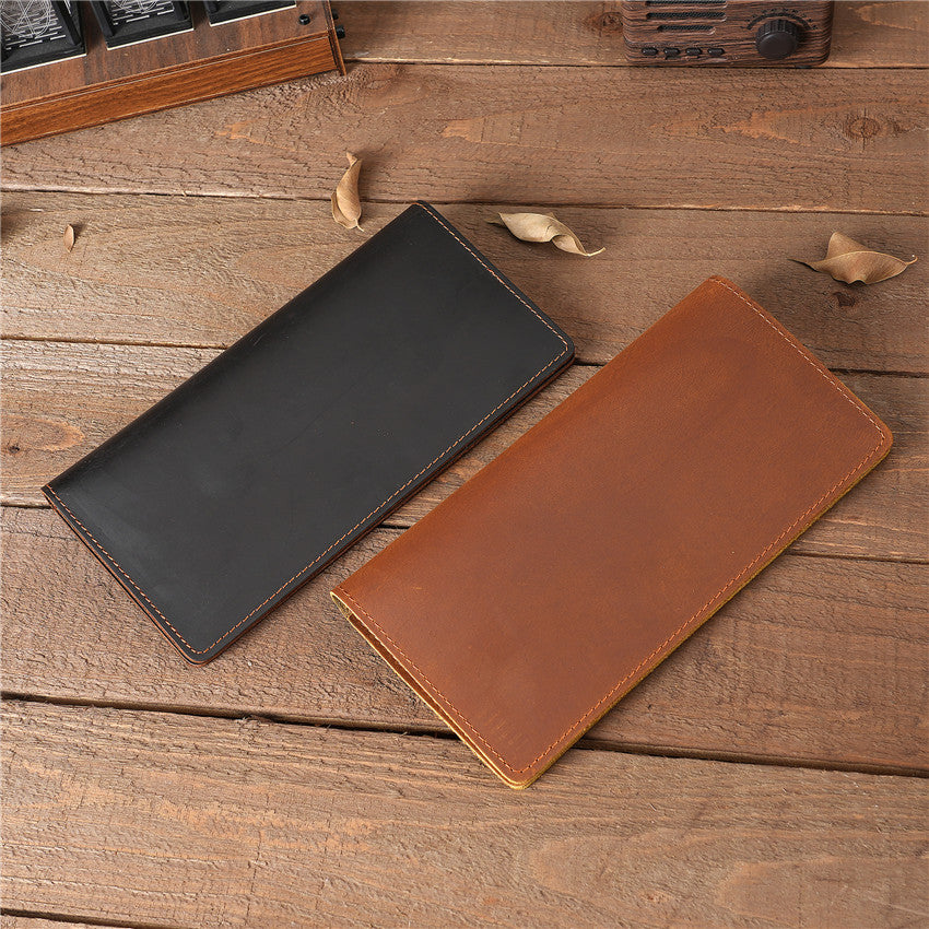 Two handmade oil waxed leather Long Snap Wallets, one black and one tan brown, displayed on a rustic wooden surface.