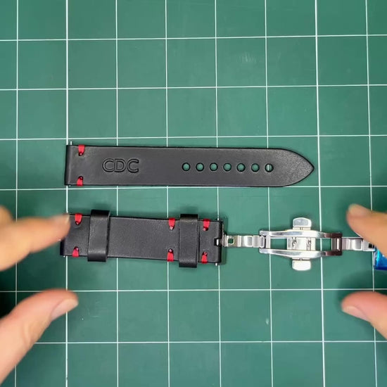 Hands assembling a custom black leather watch strap by installing a black metal hardware adapter and securing the strap to a silver butterfly clasp.