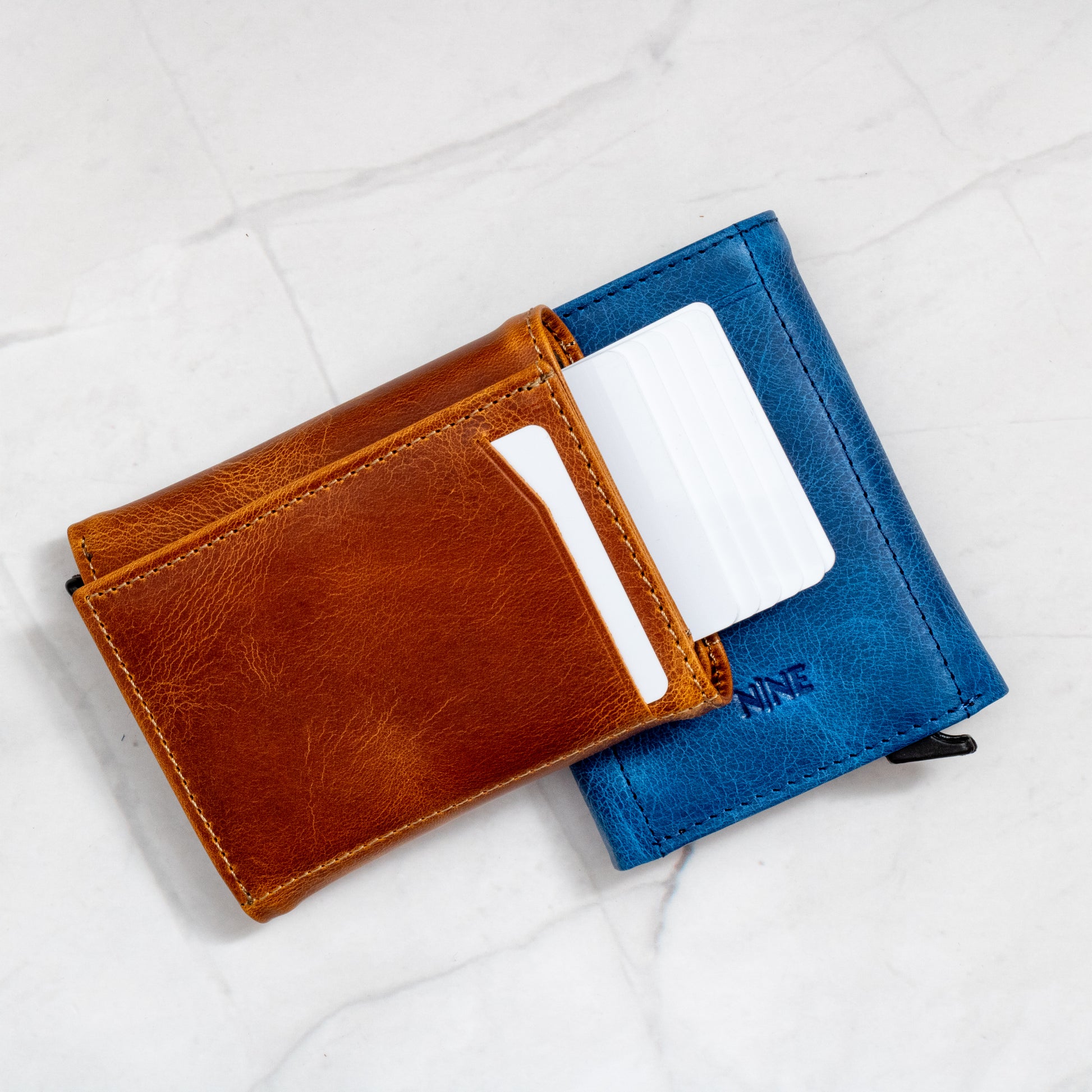 Tan Trifold Pop-Up Wallet overlapping a Blue wallet, showing the cards ejected from the mechanism.