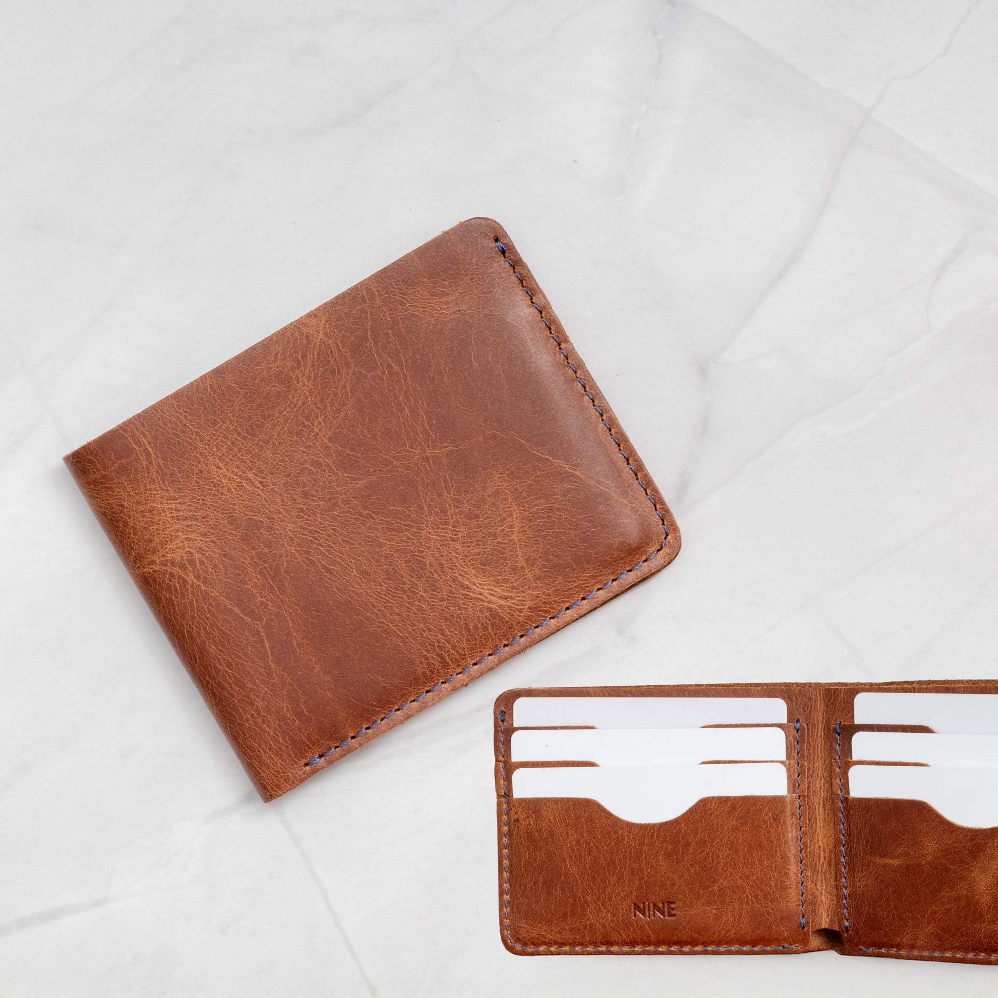 Tan Full-Grain Leather Classic Bifold Wallet exterior showing signature NINE logo and blue stitching.
