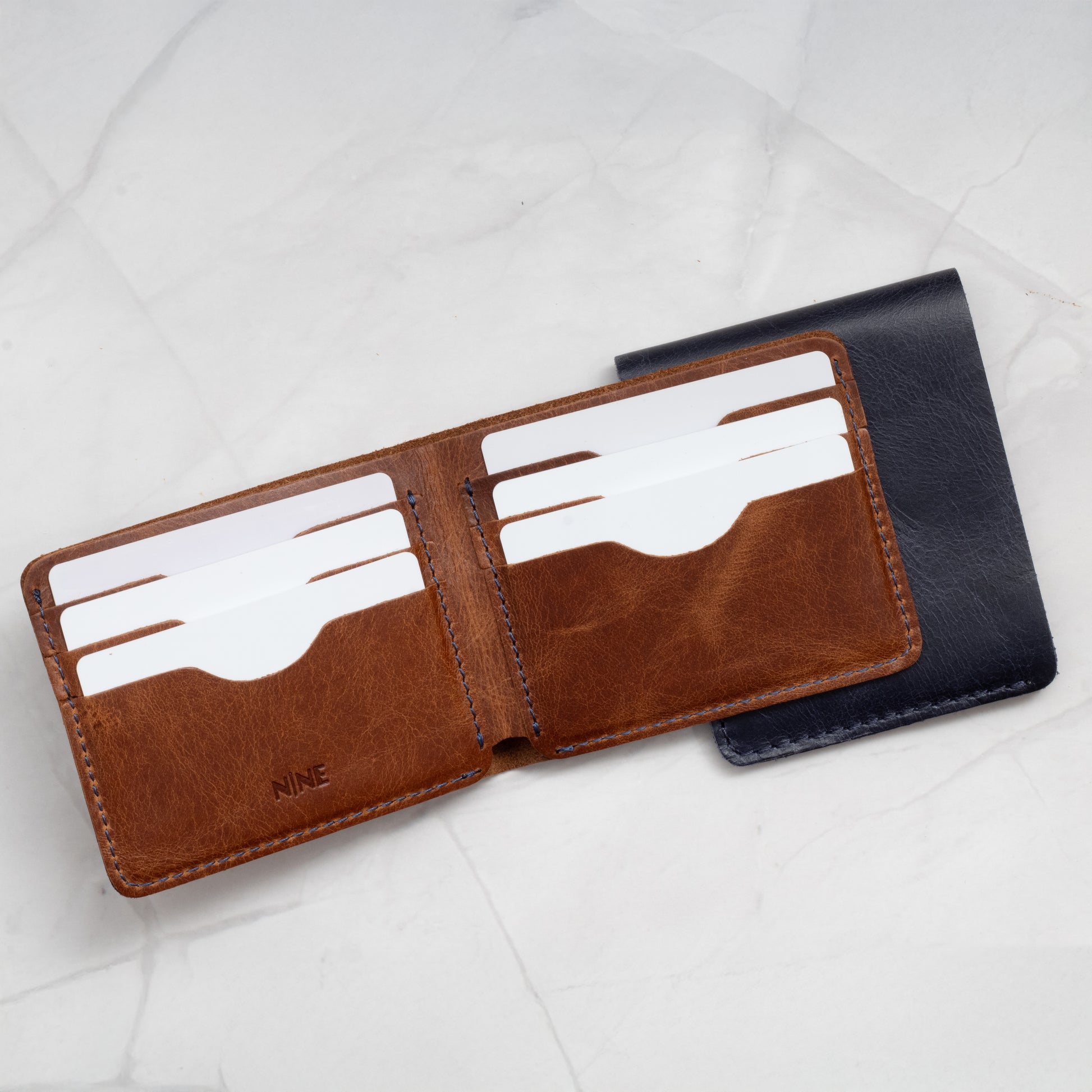 Open view of a Tan Full-Grain Leather Classic Bifold Wallet interior, showing the six card slots and blue contrast stitching.