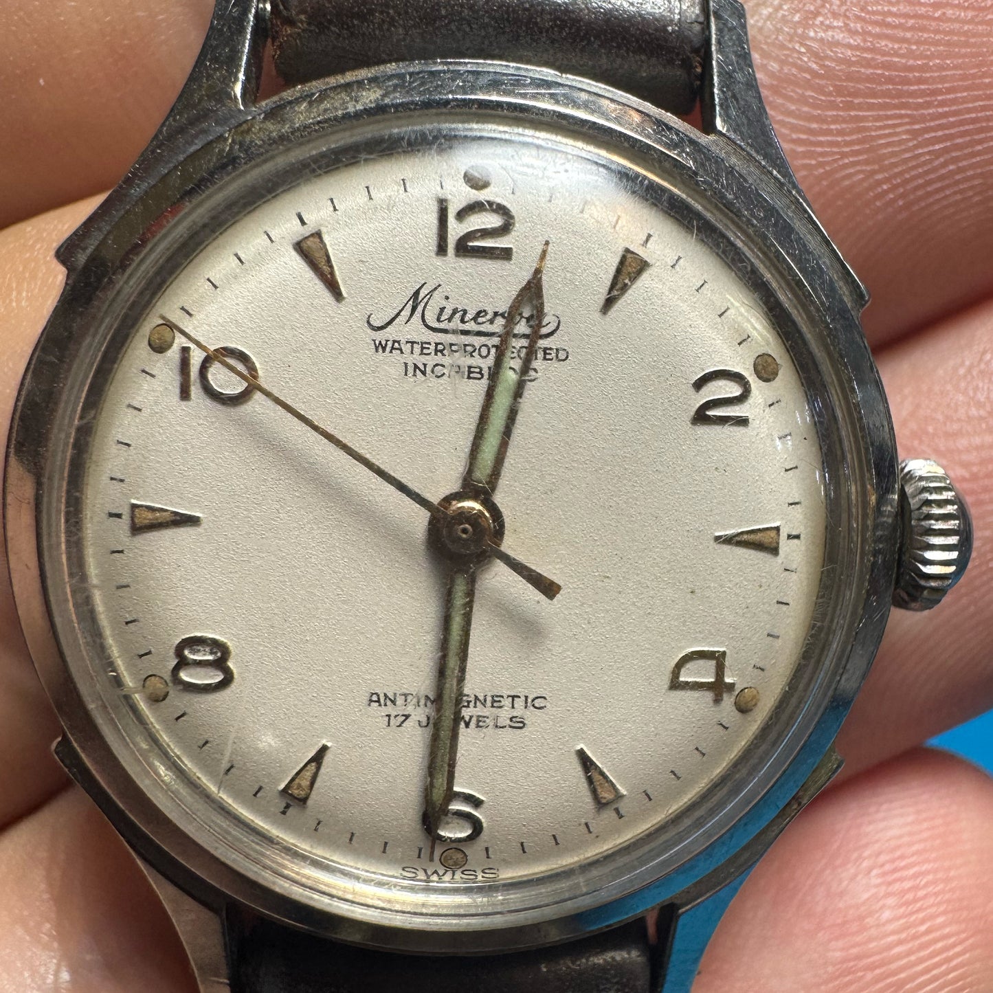 Clear, straight-on close-up of a vintage 1940s Minerva watch dial displaying Arabic numerals, syringe hands, and a beautiful vintage patina.