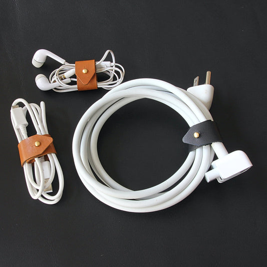 A brown leather cord wrap organizing a Macbook charger cable.