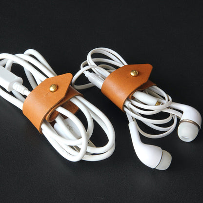 A tan brown leather cord wrap neatly organizing a pair of white headphones.