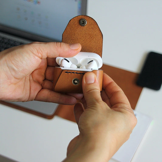 A person is holding an Apple Airpods Pro case made of tan leather, which is open and displaying the Airpods inside.